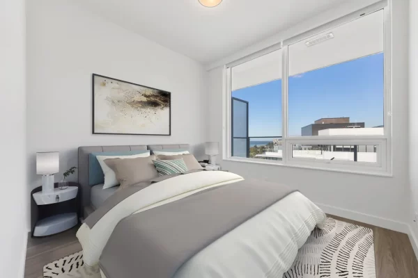 right, contemporary bedroom with hardwood floors, a large bed, and floor-to-ceiling windows showing a clear blue sky and city views at Gateway Residences.